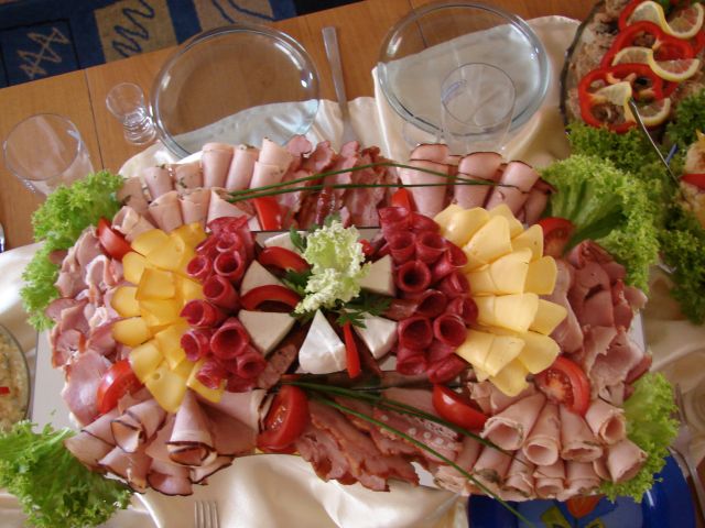 Dekoracyjnie ułożone wędliny, sery, pomidory i sałata na paterze, gotowe do serwowania na przyjęciu.