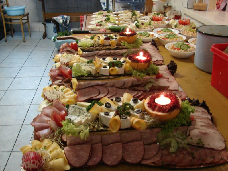 Stół z przekąskami: wędliny, sery, sałatki, dekoracje ze świecami w wydrążonych owocach, przygotowane do obsługi imprezy.