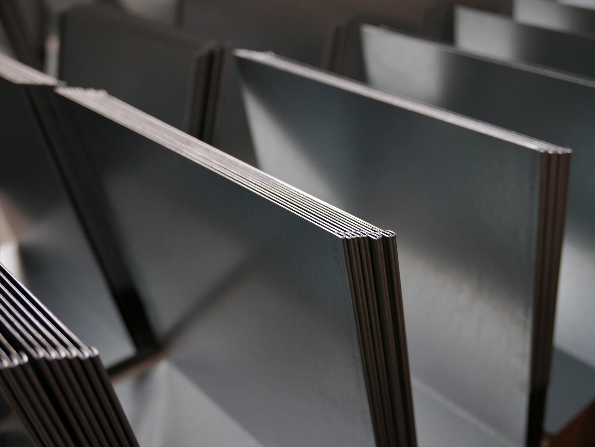 Stos arkuszy blachy o gładkiej, metalicznej powierzchni, ułożonych jeden na drugim, widoczne krawędzie i odbicia światła.