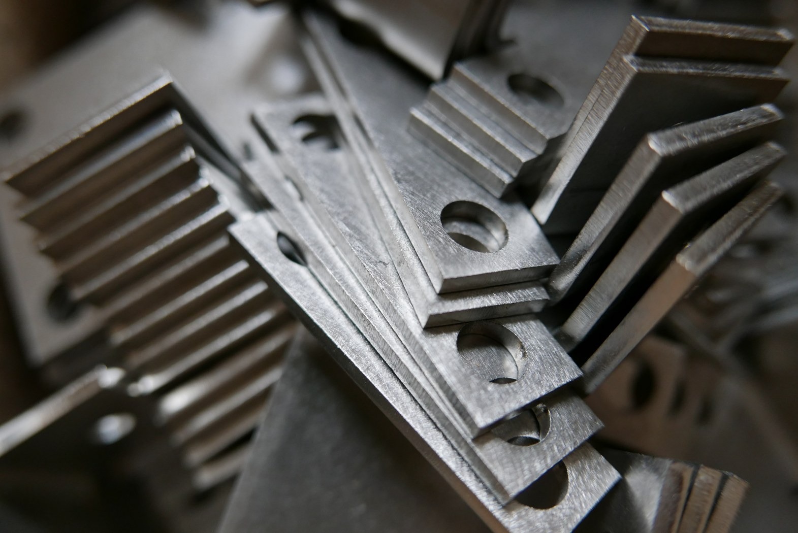 Stos obrobionych, metalowych płytek z otworem, niektóre z frezowanymi krawędziami, ułożonych pod kątem, widoczne ślady obróbki.