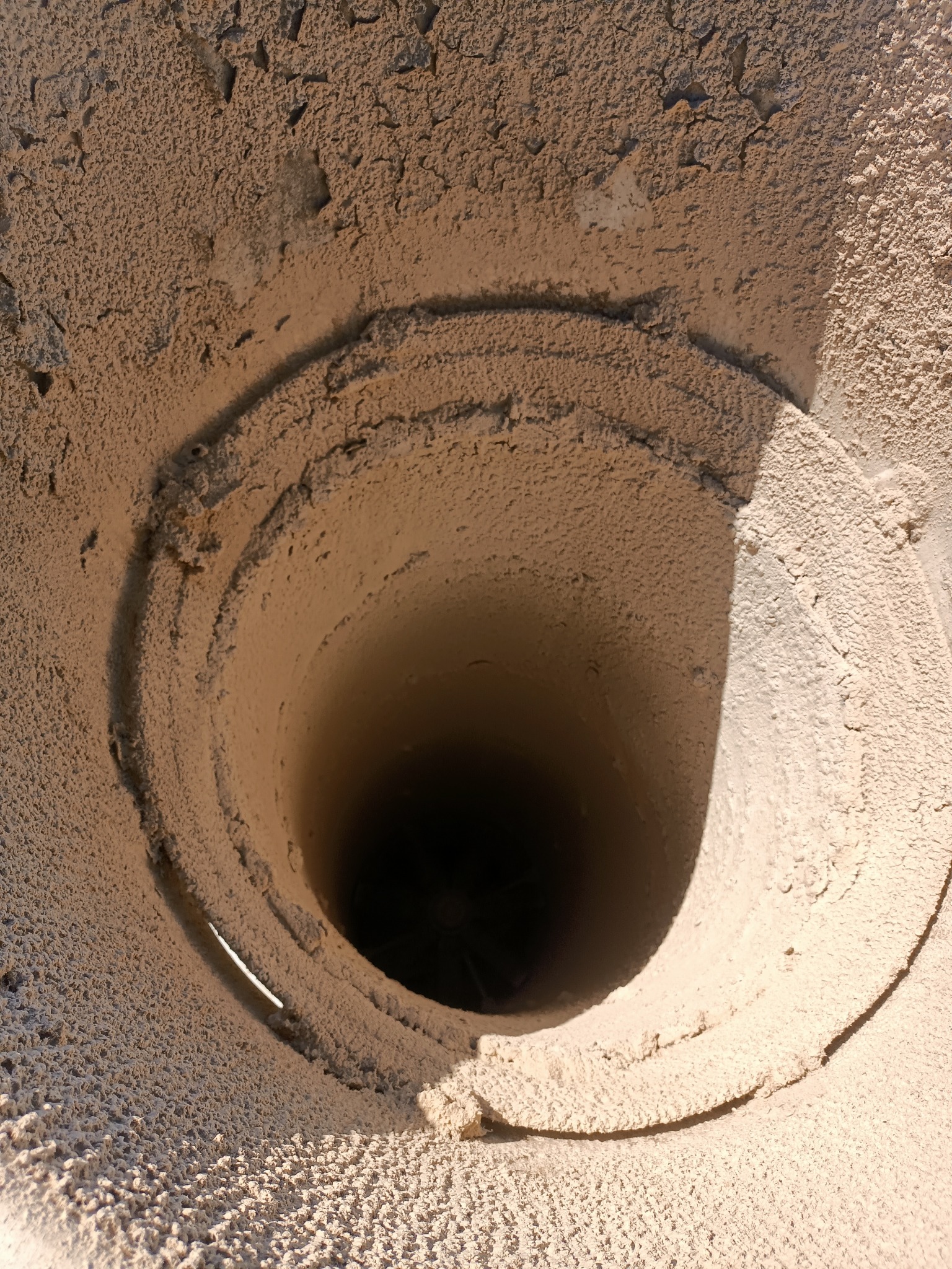 Wnętrze studzienki kanalizacyjnej pokrytej grubą warstwą piasku i ziemi, widok z góry w dół.