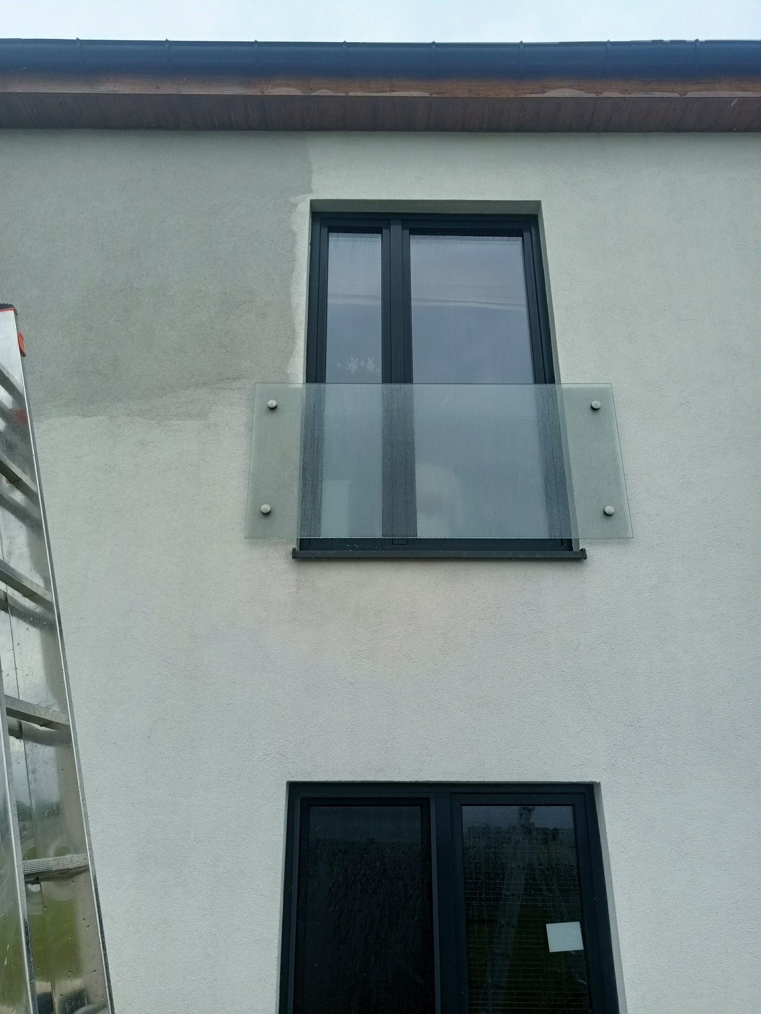 Fragment elewacji budynku w trakcie czyszczenia, widoczna drabina oparta o ścianę, górna część ściany jest czystsza od dolnej, okna z szklaną balustradą