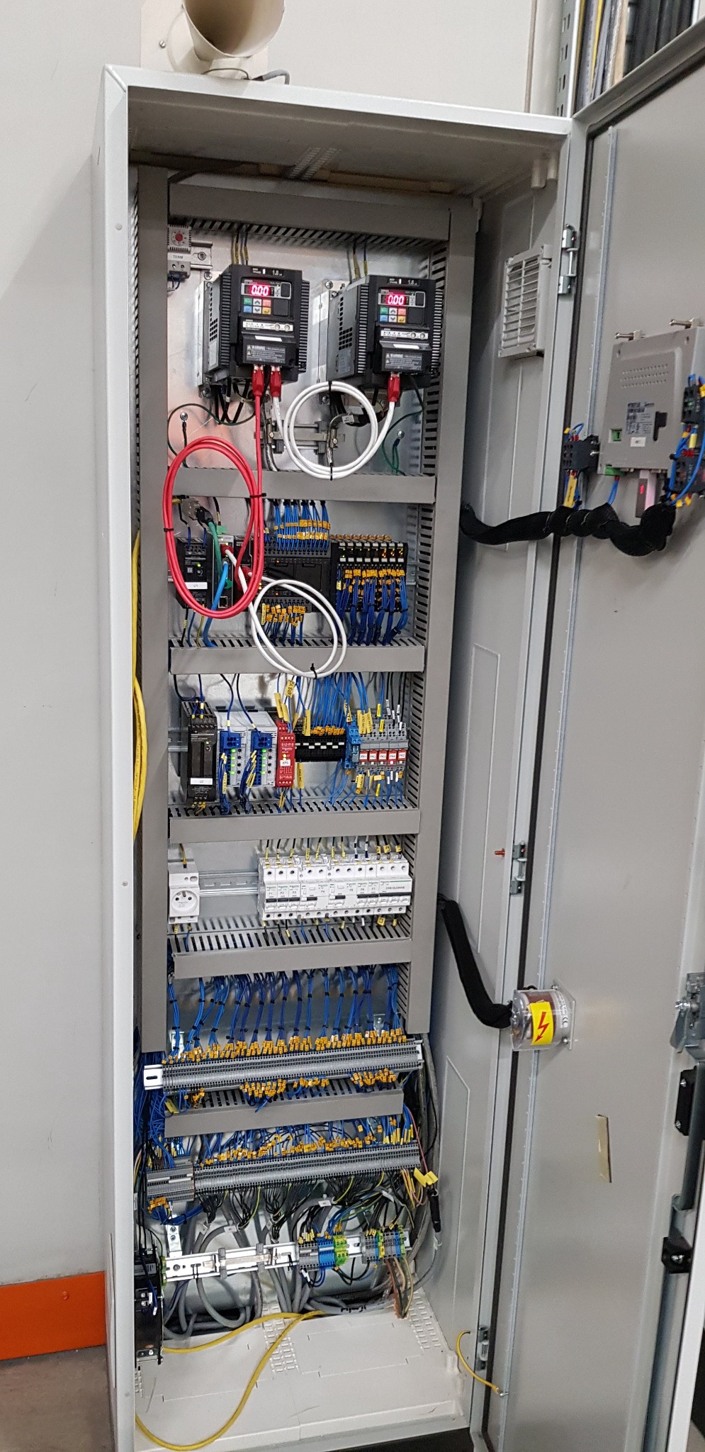 Otwarta szafa sterownicza z licznymi przewodami, modułami i zabezpieczeniami, widoczne dwa falowniki z wyświetlaczami.