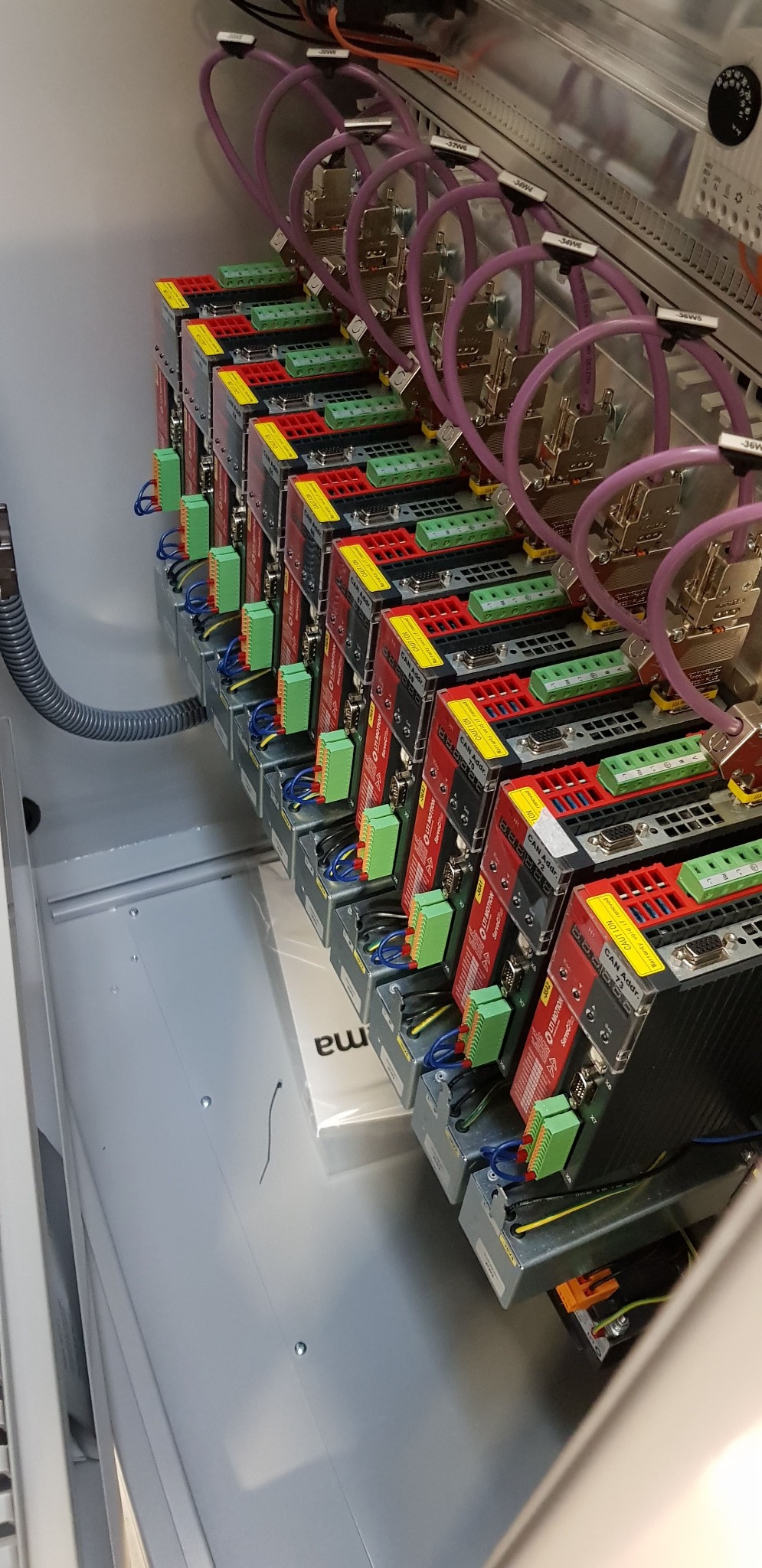 Szereg identycznych modułów sterujących, prawdopodobnie serwonapędów, zamontowanych w metalowej szafie sterowniczej, z widocznymi przewodami i złączami.