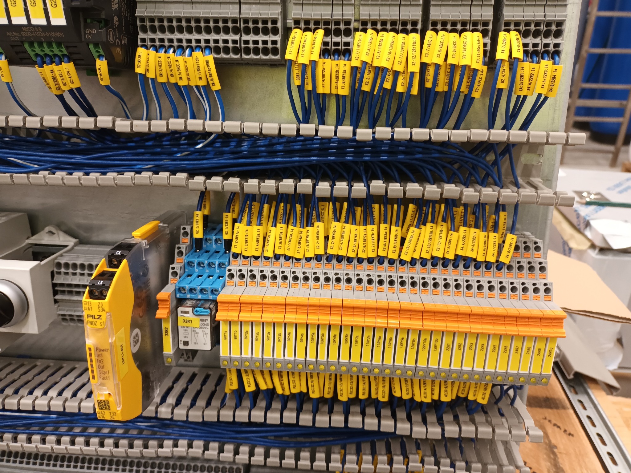 Szczegółowe ujęcie rozdzielnicy elektrycznej z licznymi niebieskimi przewodami oznaczonymi żółtymi etykietami w Siemianicach. Widoczne złącza, bezpieczniki i moduły sterujące. Skupiono się...