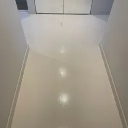 Błyszcząca, śnieżnobiała podłoga w wąskim korytarzu z lustrzanymi drzwiami szafy w tle, widoczne odbicia światła na gładkiej powierzchni.