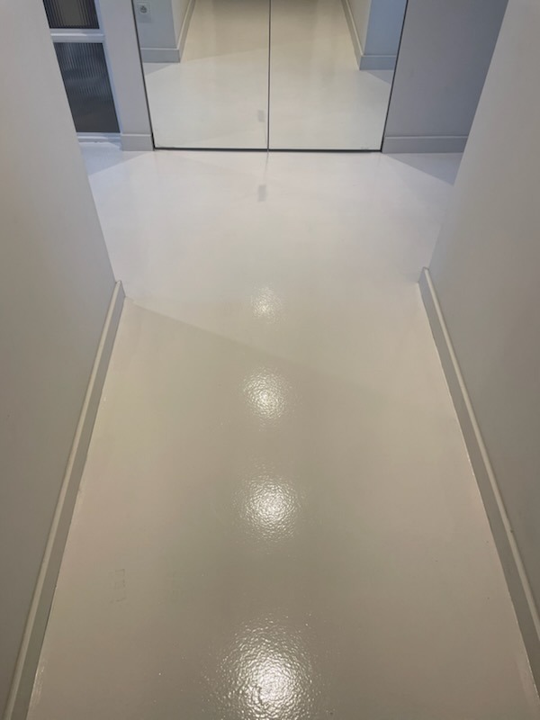 Błyszcząca, śnieżnobiała podłoga w wąskim korytarzu z lustrzanymi drzwiami szafy w tle, widoczne odbicia światła na gładkiej powierzchni.