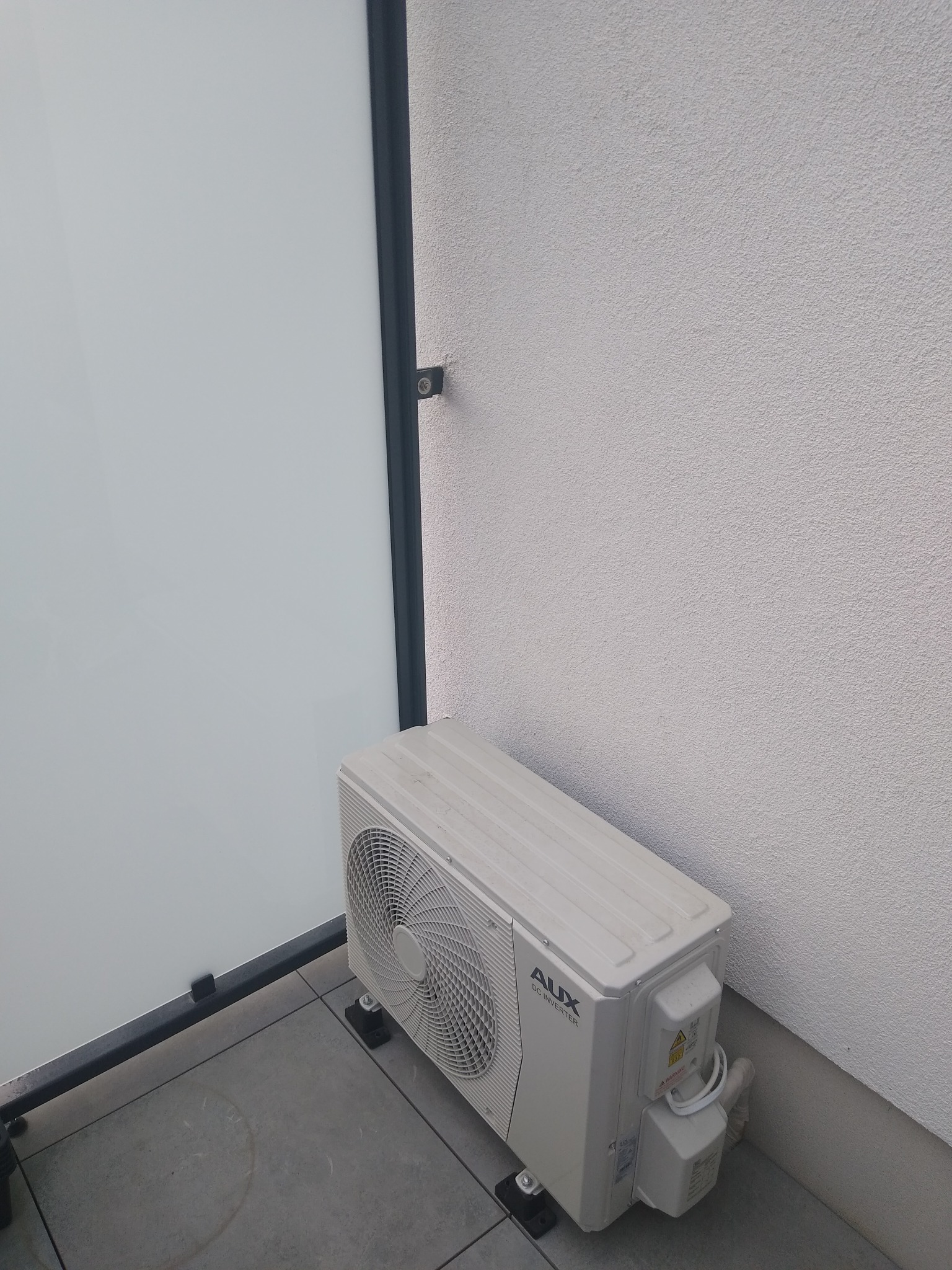 Zewnętrzna jednostka klimatyzacji AUX zamontowana na balkonie, widoczne przyłącza i elementy konstrukcyjne.