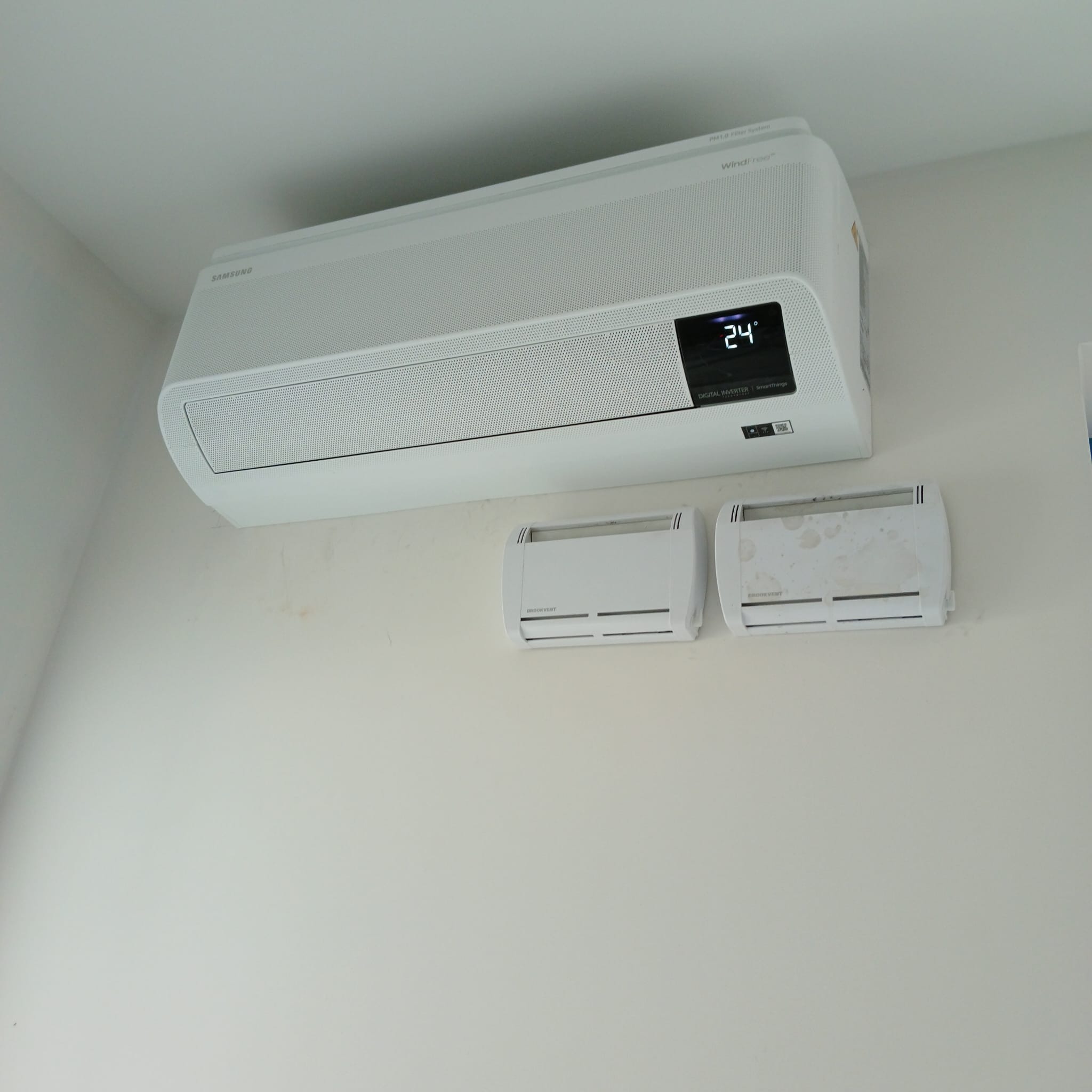 Biała jednostka wewnętrzna klimatyzacji Samsung WindFree zamontowana na ścianie, z dwoma mniejszymi nawiewnikami poniżej, jeden z nich jest zabrudzony.