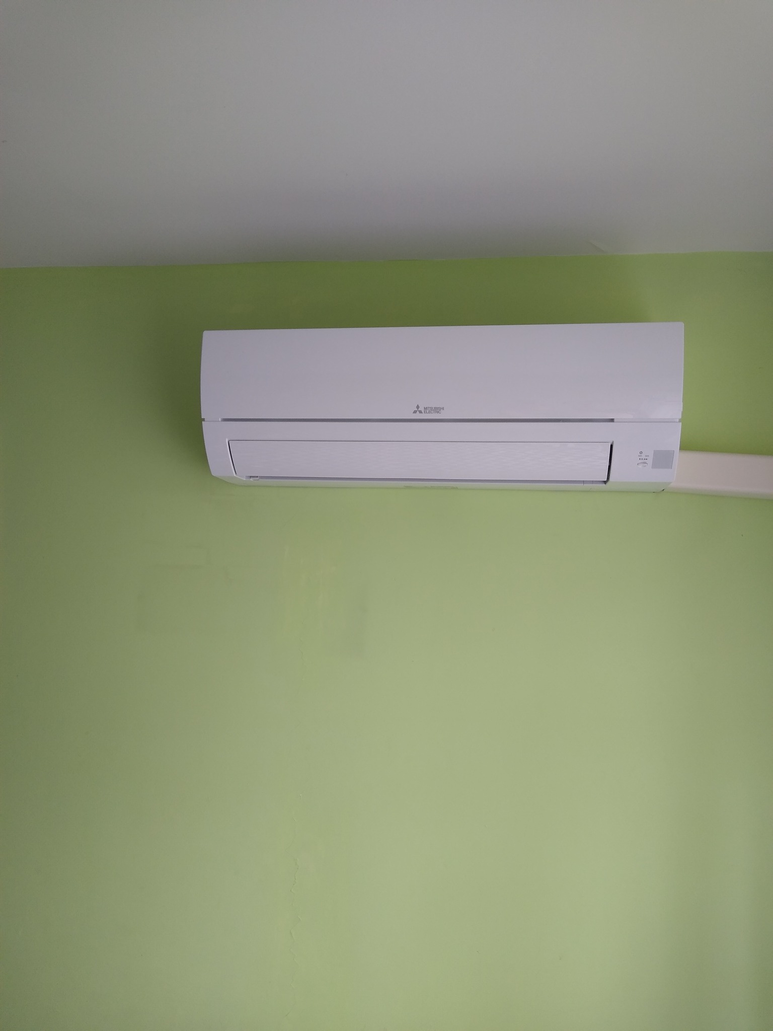 Biały klimatyzator Mitsubishi Electric zamontowany na zielonej ścianie. Widok z dołu, oświetlenie dzienne.