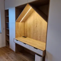 Biało-drewniana szafa na wymiar z wbudowanym biurkiem i oświetleniem LED w kształcie domku, na podłodze parkiet.