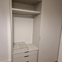 Wnętrze szafy wnękowej z przesuwnymi drzwiami, szufladami i półkami, wykończone w odcieniach szarości, z widoczną szufladą na biżuterię z przeszklonym wiekiem.