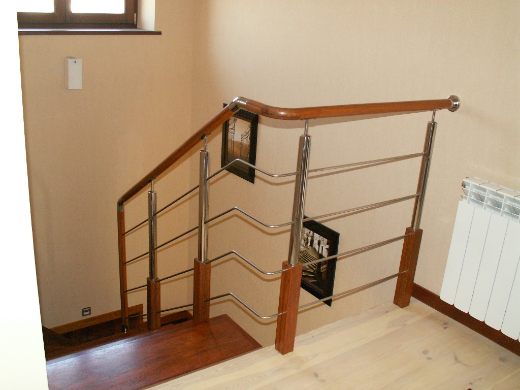 Nowoczesna balustrada schodowa ze stali nierdzewnej i drewna, z poziomymi prętami, zamontowana na drewnianych schodach, widoczne obrazy w czarnych ramkach na ścianie.