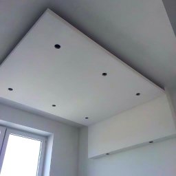 RemontLux - Nowoczesny, biały sufit podwieszany z punktowym oświetleniem LED, widok z dołu, ukośnie, widać fragment okna i ściany.