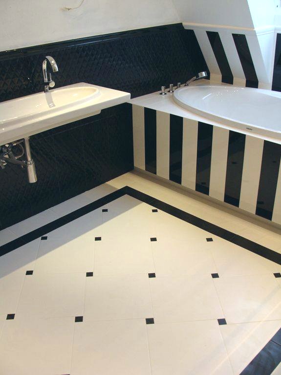 Biało-czarna łazienka z wanną w pasy, umywalką na tle czarnej ściany z wzorem i podłogą z białych płytek z czarnymi akcentami.