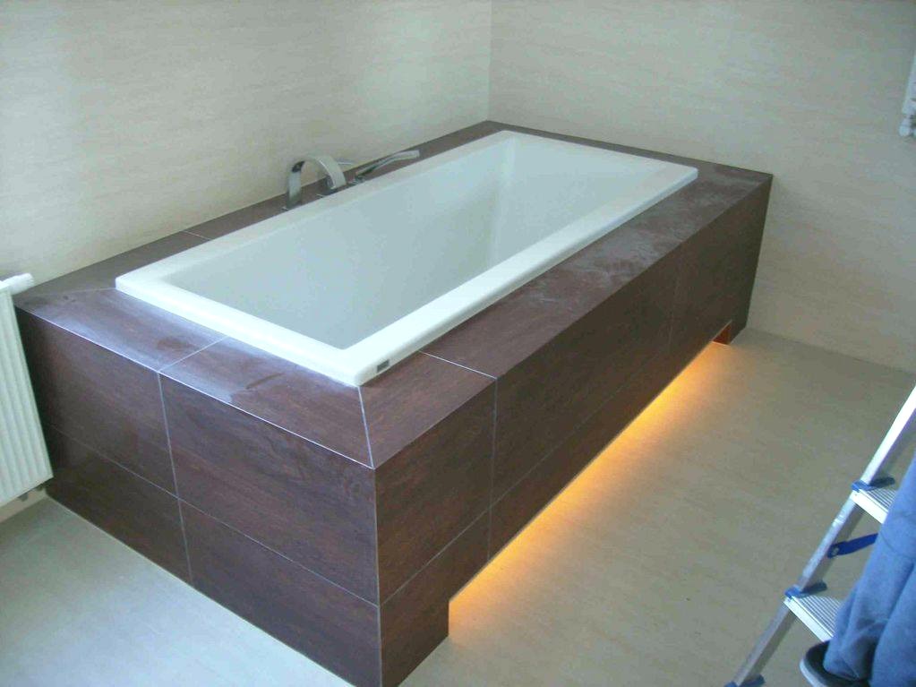 Wanna obudowana ciemnobrązowymi płytkami, z podświetleniem LED u dołu, widoczna drabina z fragmentem spodni w rogu