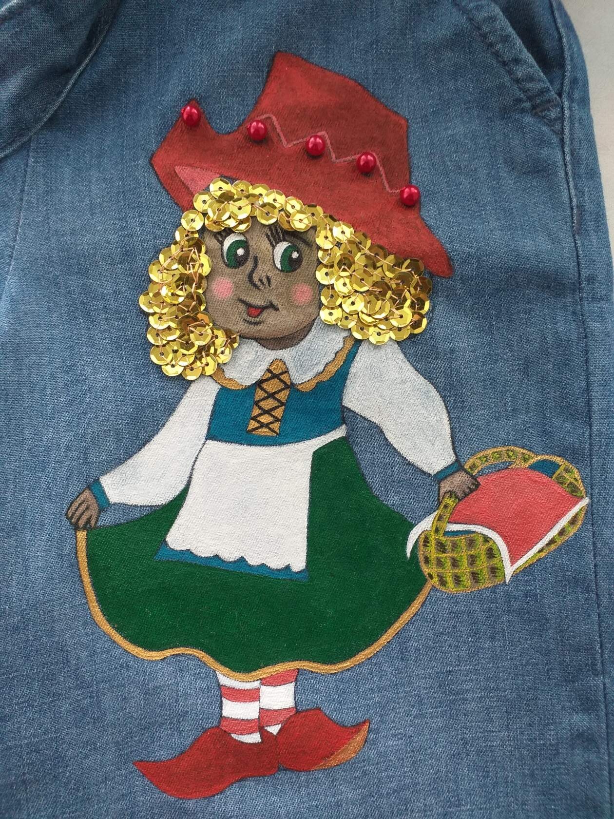 Ręcznie malowana postać dziewczynki w czerwonym kapeluszu z cekinowymi włosami, trzymająca koszyk, na denimowej tkaninie.