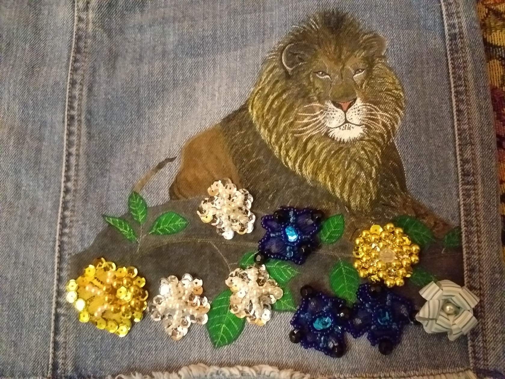 Dżinsowa kurtka z ręcznie malowanym lwem i aplikacjami z cekinowych kwiatów w odcieniach złota, bieli i granatu.