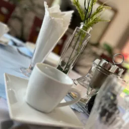 Elegancko nakryty stół z białą porcelaną, szklanym wazonem z białymi kwiatami, przyprawnikiem i serwetkami, przygotowany do przyjęcia gości.