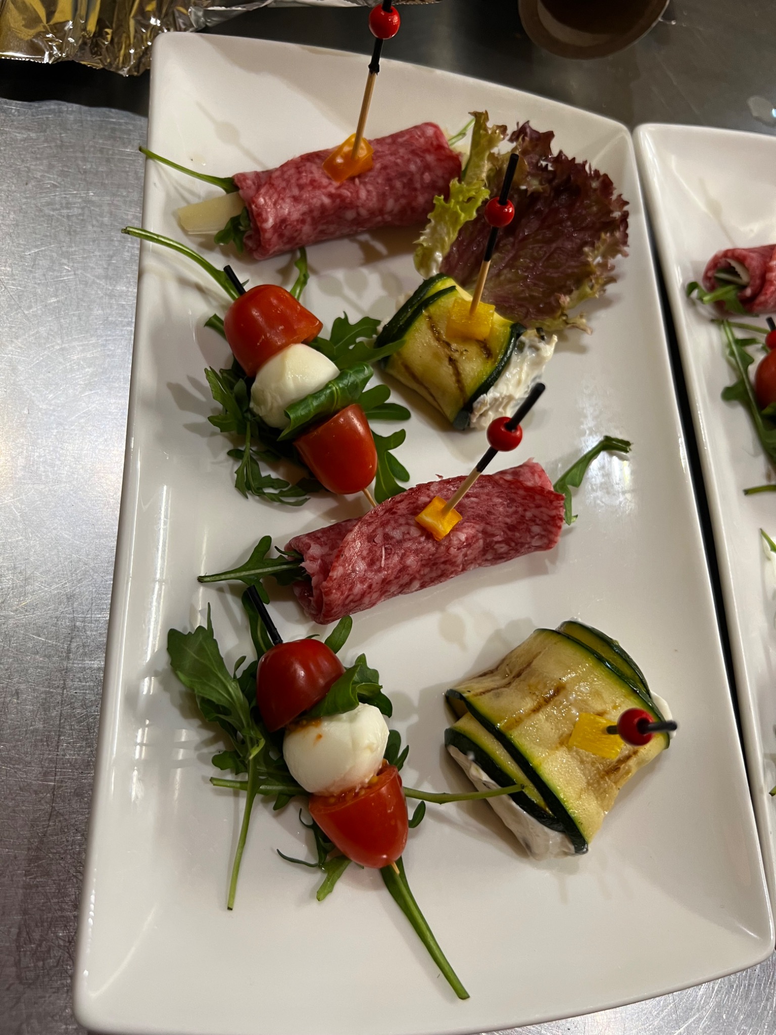 Elegancko podane przekąski na białym talerzu z salami, mini-mozzarellą i grillowaną cukinią, przygotowane przez firmę cateringową z Siemianowic Śląskich.