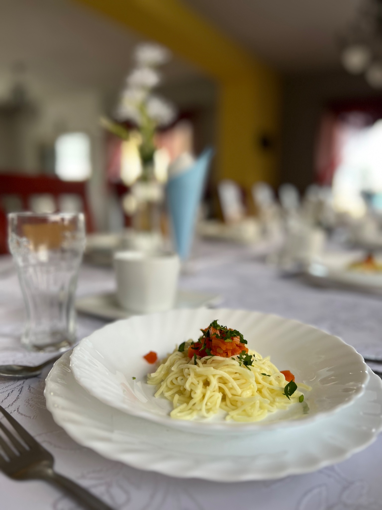 Elegancko podane spaghetti z warzywami na białym talerzu, część zastawy stołowej i dekoracje w tle, ujęcie z bliska.