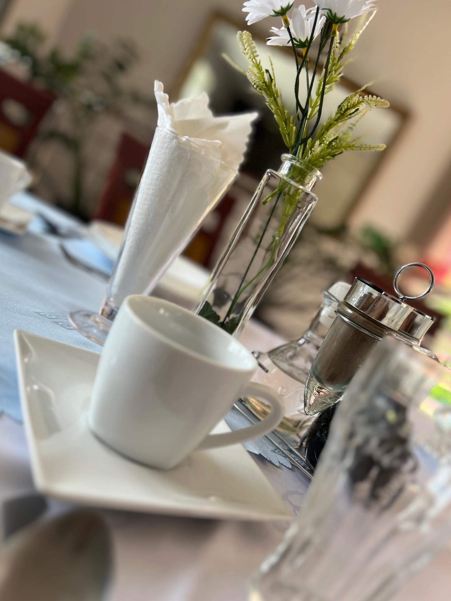 Elegancko nakryty stół z białą porcelaną, szklanym wazonem z białymi kwiatami, przyprawnikiem i serwetkami, przygotowany do przyjęcia gości.