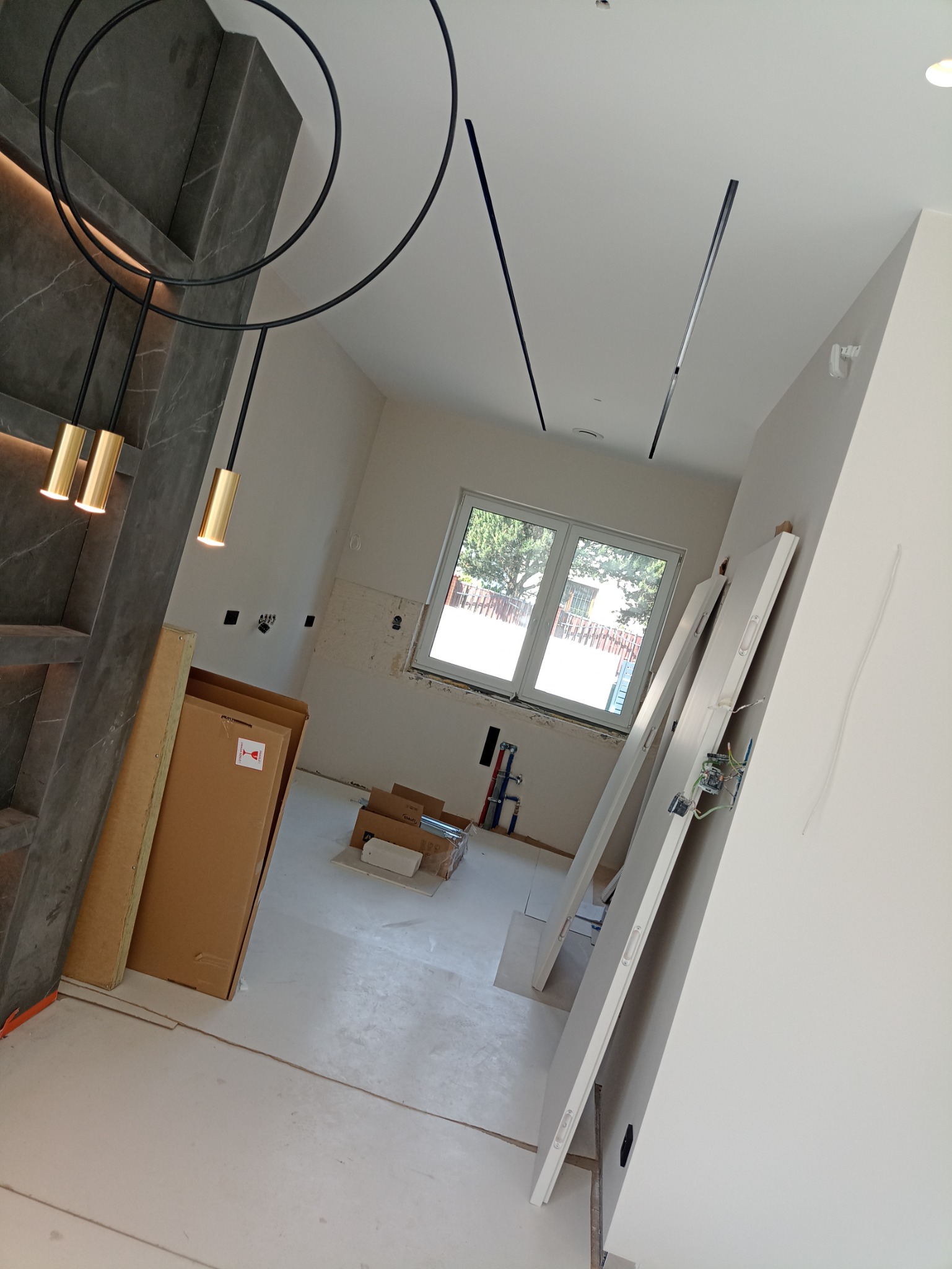 Wnętrze w trakcie remontu: widoczne elementy oświetlenia sufitowego, kartony z materiałami budowlanymi, białe drzwi opierające się o ścianę oraz przygotowane ściany do malowania z widocznymi...