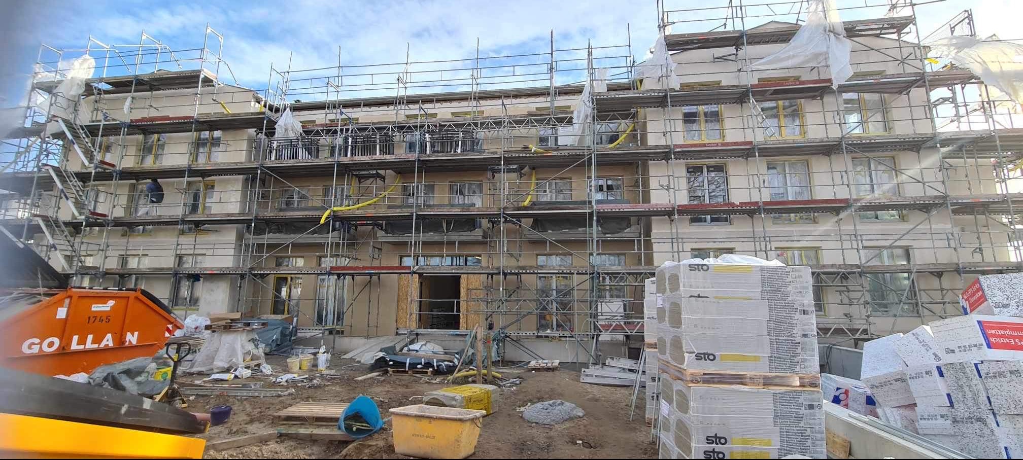 Wielopiętrowy budynek w trakcie prac elewacyjnych, widoczne rusztowania, materiały izolacyjne STO oraz kontener na odpady GOLLAN.