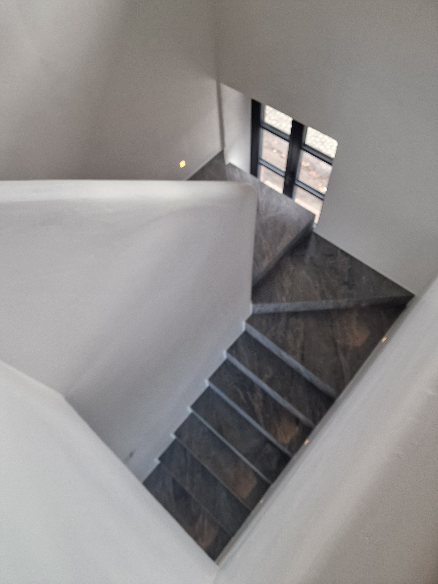 Nowoczesne schody z szarego kamienia w Mrągowie, widok z góry. Białe ściany i okno w tle. Minimalistyczny design.