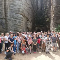 Duża grupa turystów pozuje do zdjęcia na tle skalnych formacji z tunelem w tle, w słoneczny dzień.