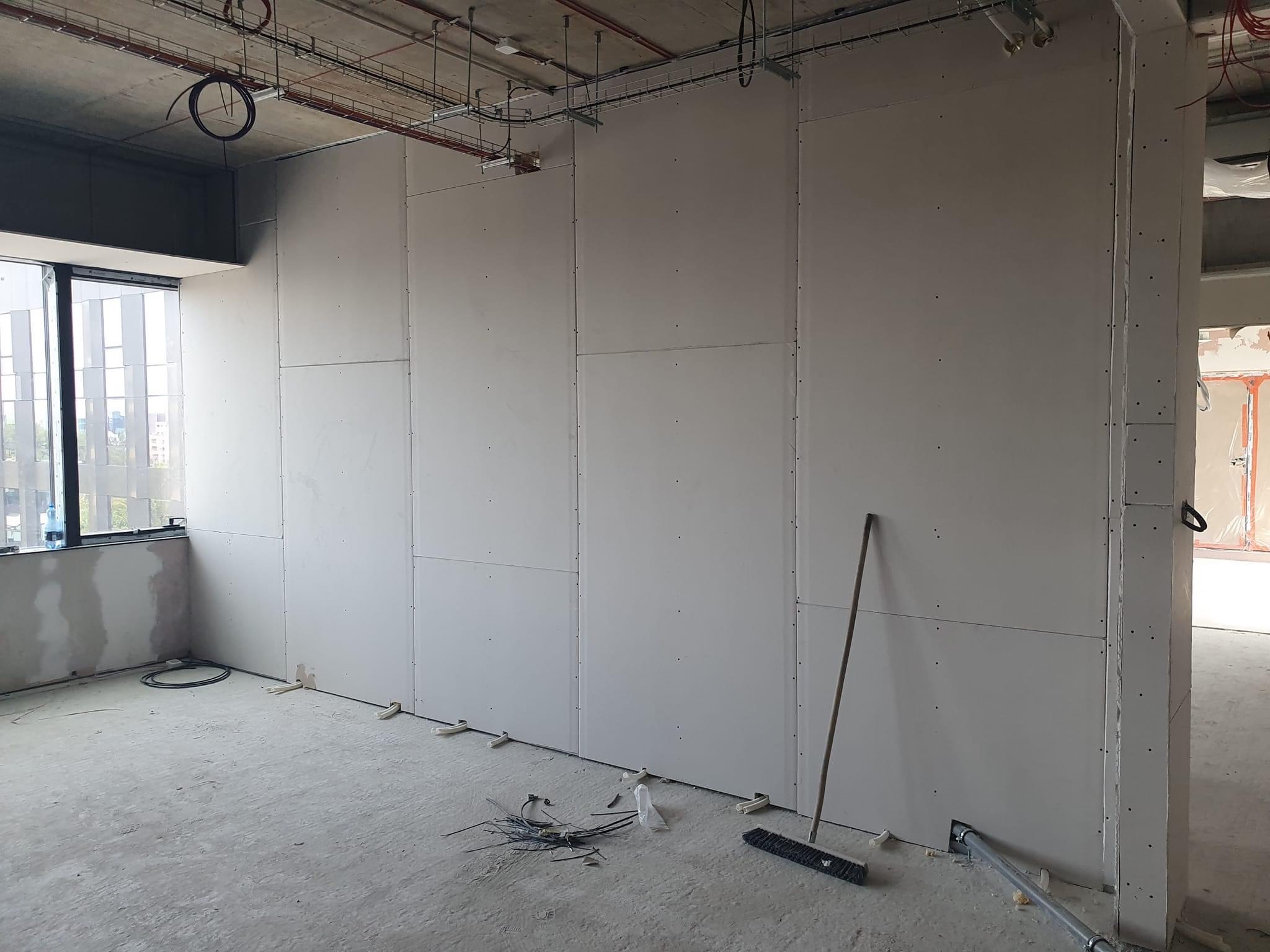 Wnętrze w trakcie prac wykończeniowych: ściany z płyt gipsowo-kartonowych, widoczne przewody elektryczne na podłodze i instalacje pod sufitem, przygotowane do dalszych prac.