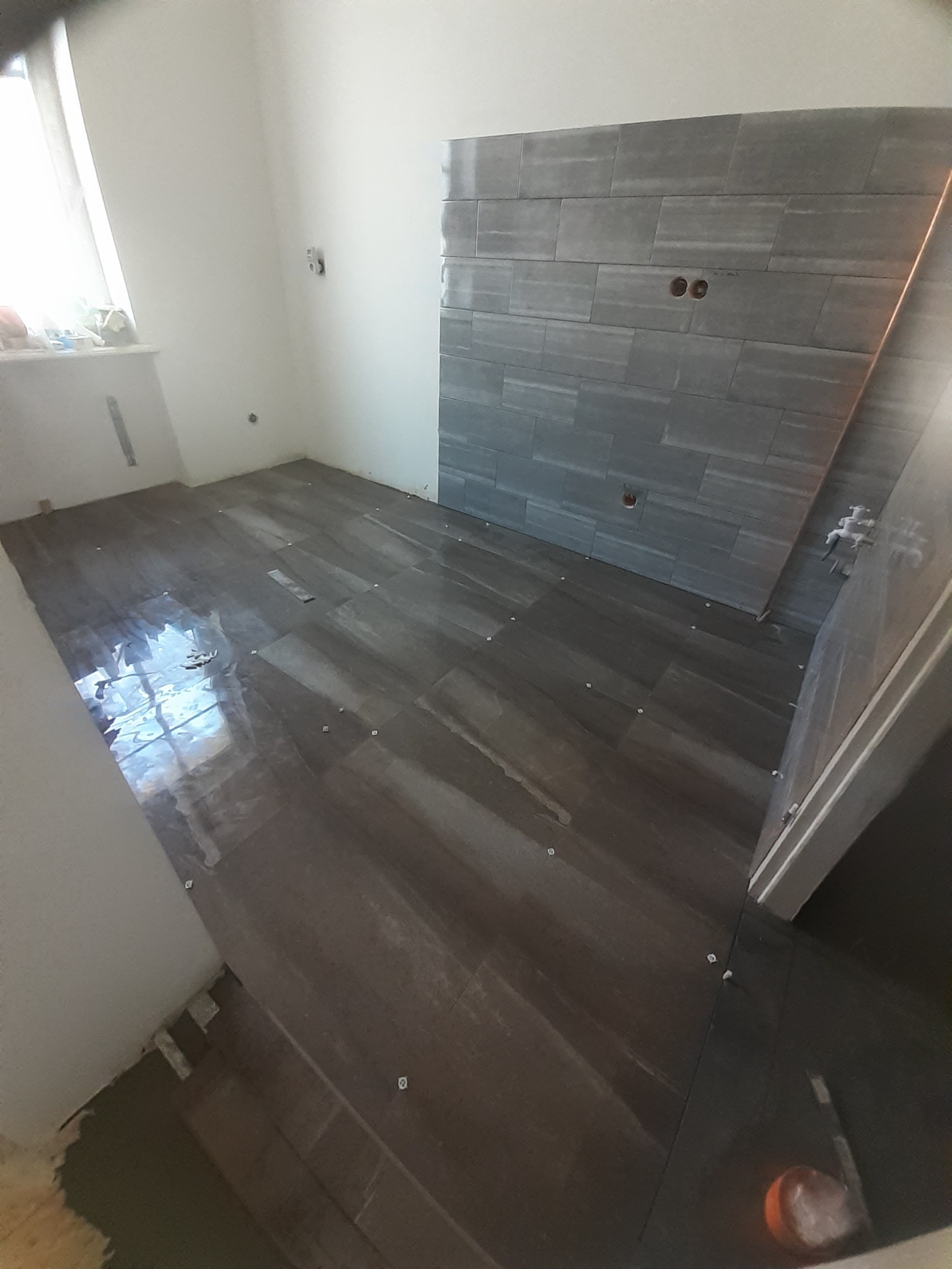 Montaż płytek podłogowych i ściennych w łazience, widoczne krzyżyki dystansowe i otwory na instalacje.