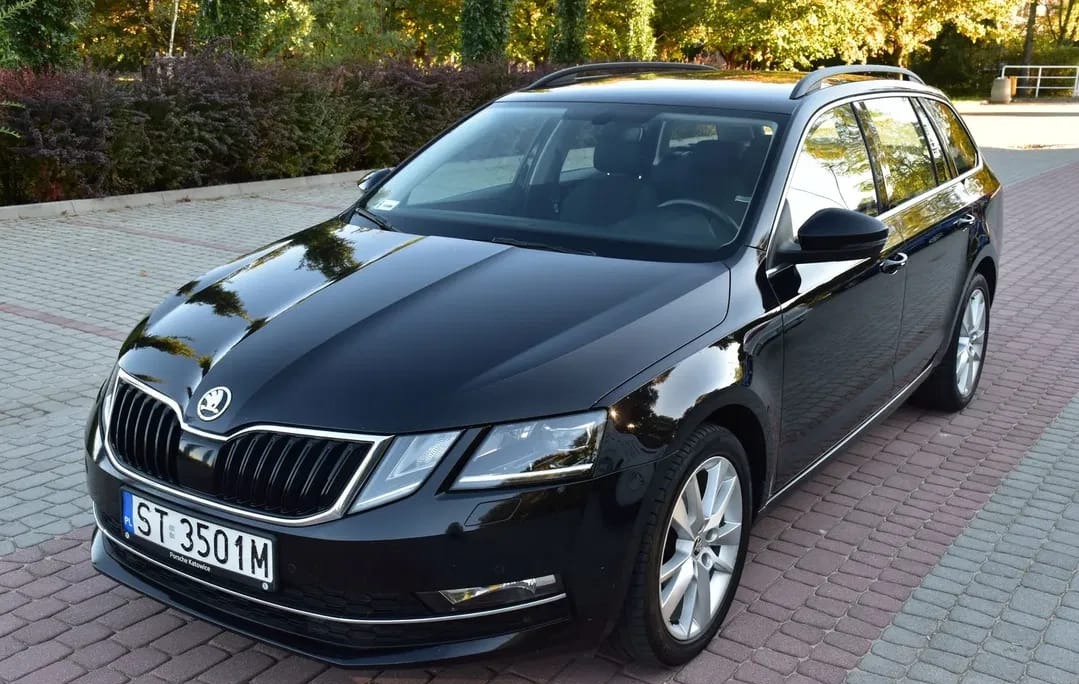 Czarna Skoda Octavia Combi, zaparkowana na brukowanym podjeździe, z widoczną tablicą rejestracyjną ST 3501M i odbiciami w karoserii.