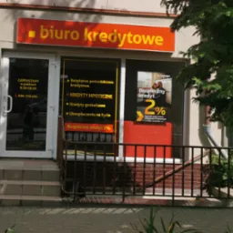 Fasada biura kredytowego z pomarańczowym szyldem i ofertami kredytów hipotecznych, gotówkowych i ubezpieczeń na szybach.