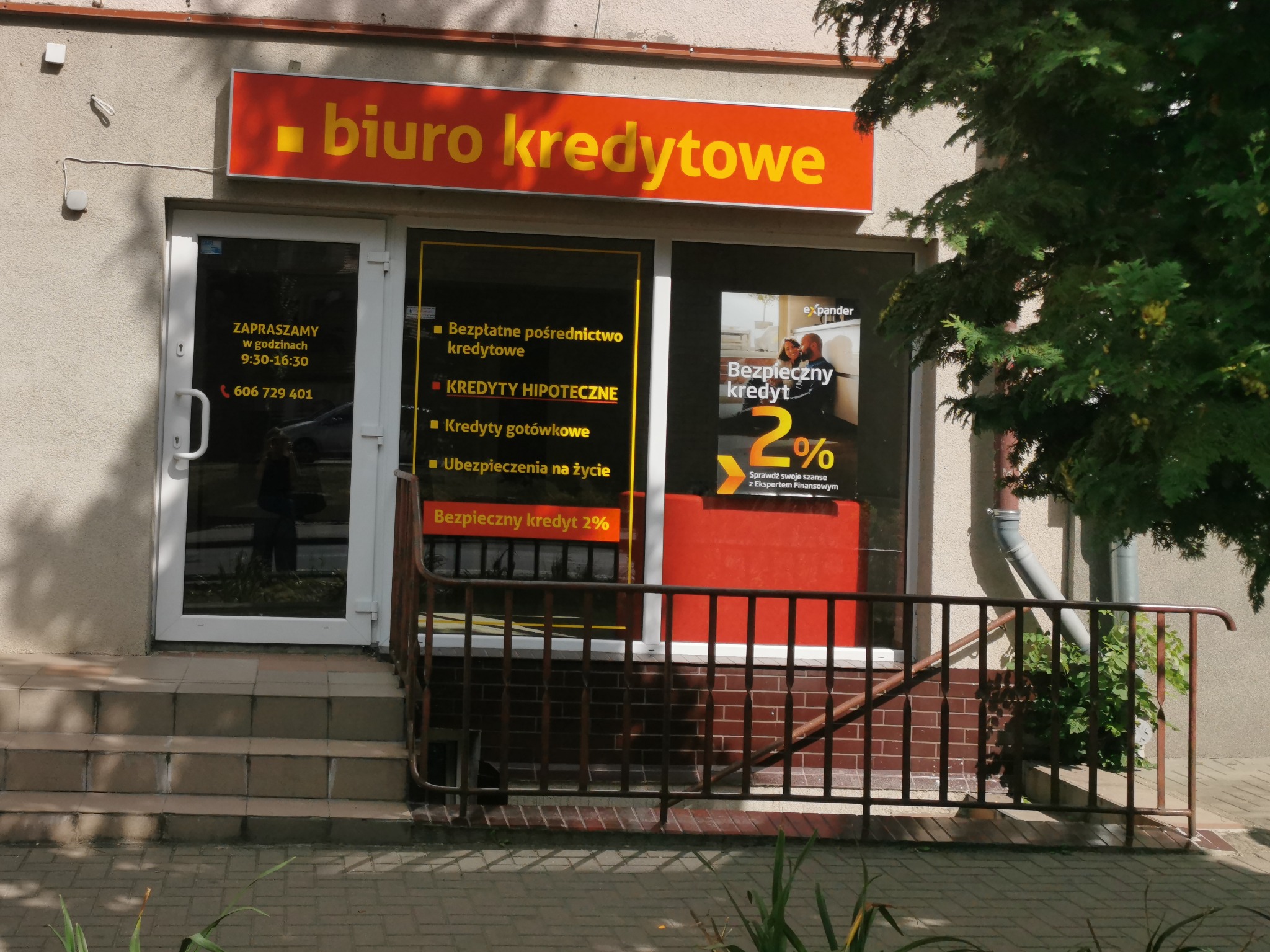 Fasada biura kredytowego z pomarańczowym szyldem i ofertami kredytów hipotecznych, gotówkowych i ubezpieczeń na szybach.