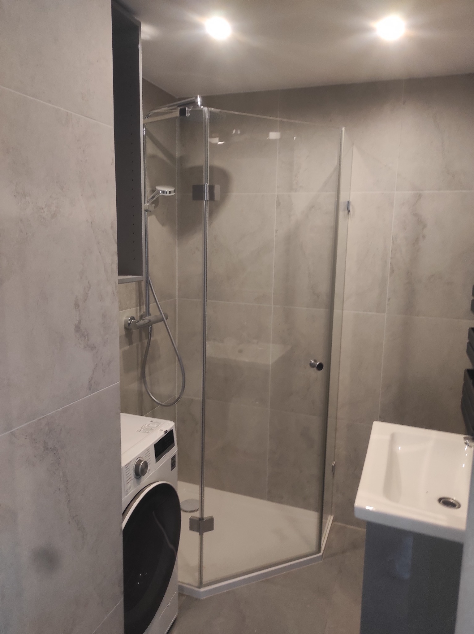 Nowoczesna łazienka w szarościach z kabiną prysznicową narożną, pralką i umywalką nablatową na szafce.