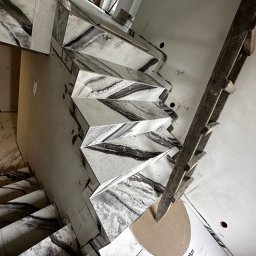 REMONT Z PASJĄ Patryk Kik - Montaż marmurowych płytek na schodach z użyciem drewnianej konstrukcji wsporczej i opakowania po płytkach. Widok z góry, podkreślający wzór kamienia.