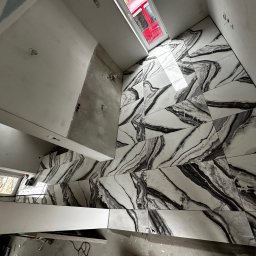 REMONT Z PASJĄ Patryk Kik - Ukończona podłoga z płytek imitujących marmur w łazience z oknem dachowym. Częściowo wykończone ściany. Widoczna instalacja elektryczna.