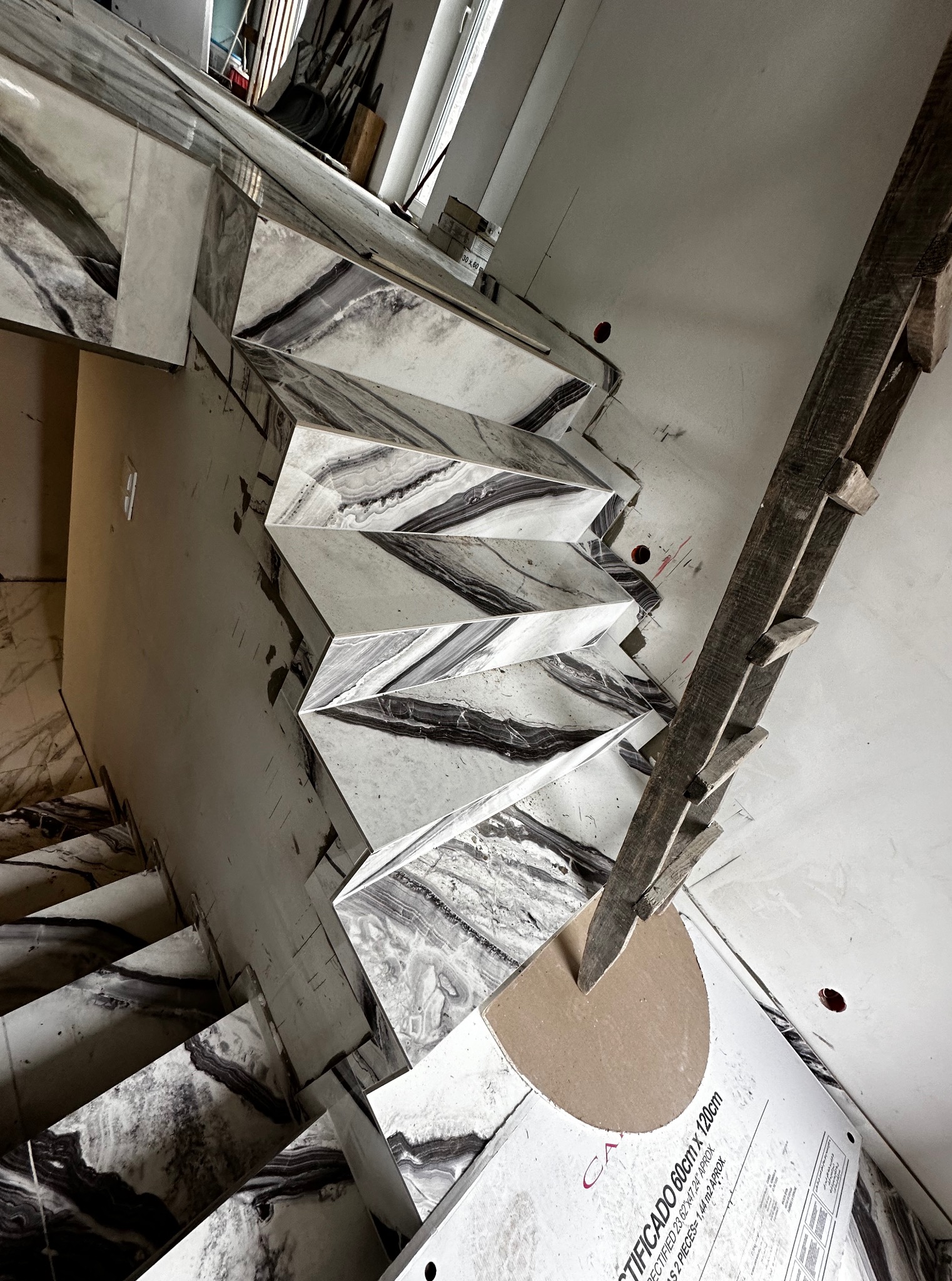 Montaż marmurowych płytek na schodach z użyciem drewnianej konstrukcji wsporczej i opakowania po płytkach. Widok z góry, podkreślający wzór kamienia.