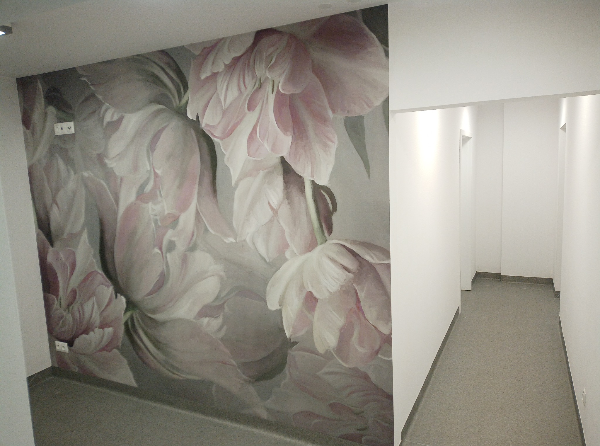 Korytarz z fototapetą w kwiaty tulipanów. Szara podłoga i białe ściany. Widoczne gniazdka elektryczne na fototapecie. Ujęcie z perspektywy wejścia do korytarza.