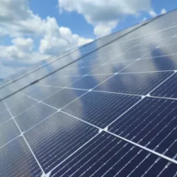 Panel fotowoltaiczny z widocznym odbiciem chmur na niebieskim niebie, zainstalowany na dachu.