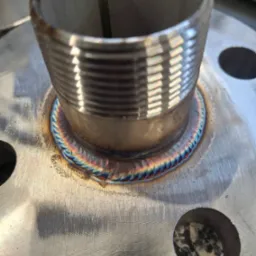 Precyzyjne połączenie spawane rury gwintowanej z metalową płytą, widoczne tęczowe zabarwienie spoiny, świadczące o wysokiej jakości wykonania.