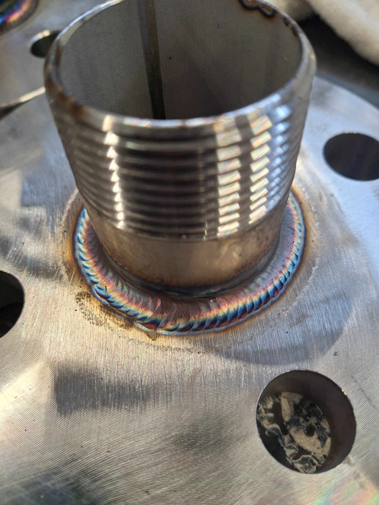 Precyzyjne połączenie spawane rury gwintowanej z metalową płytą, widoczne tęczowe zabarwienie spoiny, świadczące o wysokiej jakości wykonania.