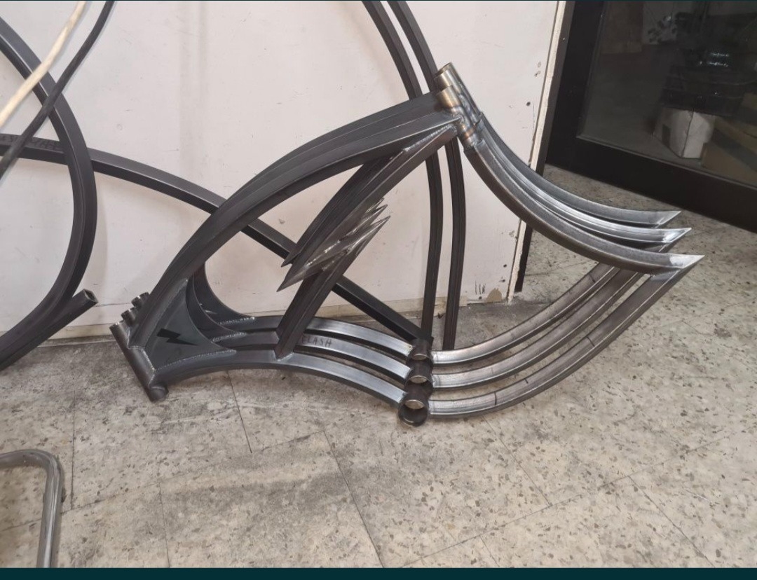 Metalowa konstrukcja z profili, spawana, z elementami dekoracyjnymi w kształcie błyskawic. Surowy stan, widoczne spawy i niedoskonałości. Nietypowy projekt.