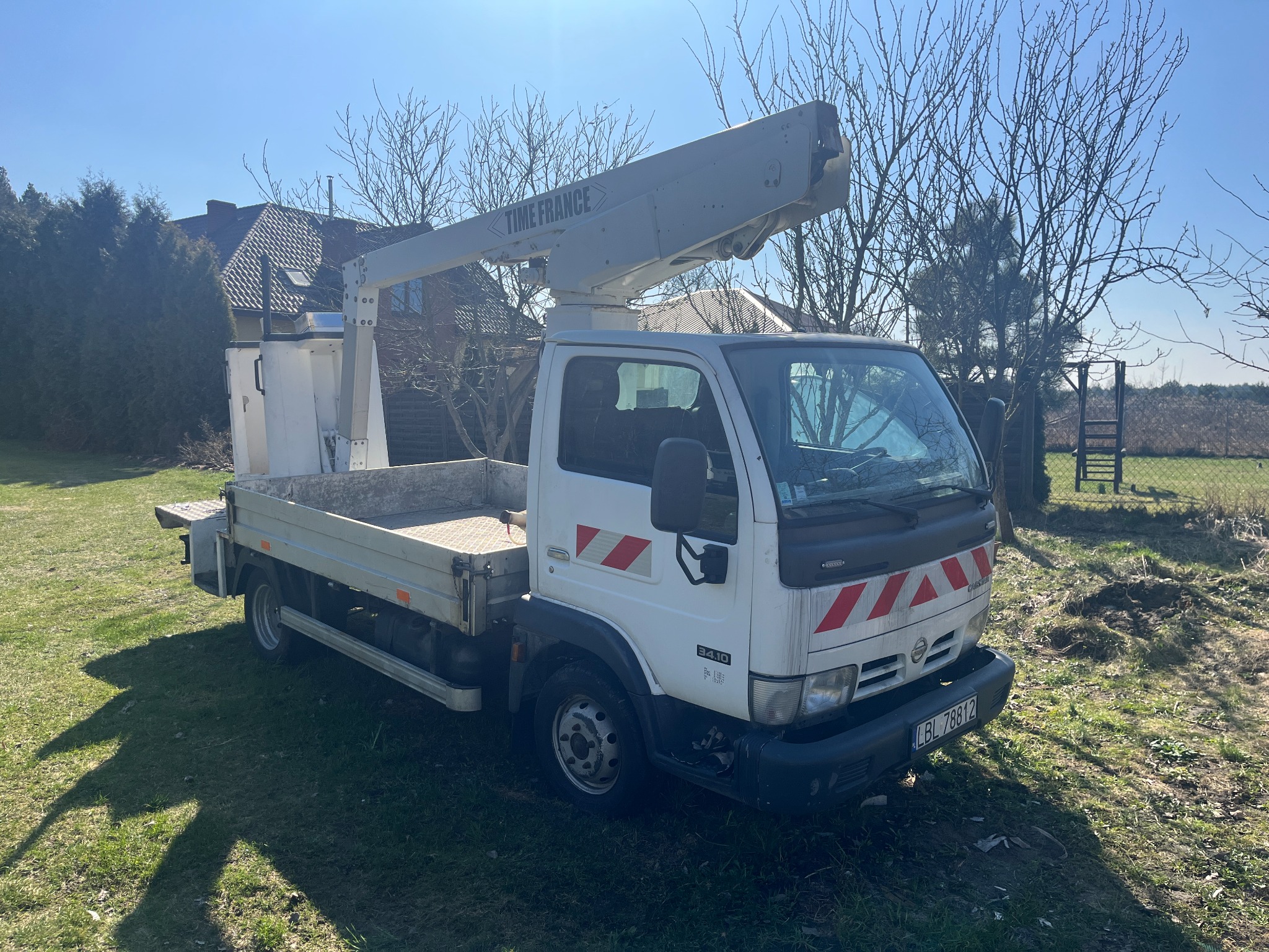 Biała platforma montażowa marki Time France na podwoziu Nissan Cabstar, zaparkowana na trawniku w słoneczny dzień.