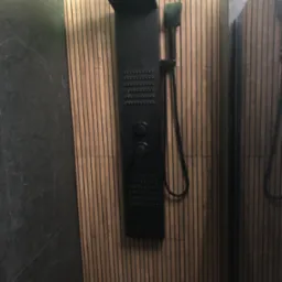 Nowoczesny panel prysznicowy w kolorze czarnym, zamontowany na ścianie wykończonej drewnianymi lamelami w kabinie prysznicowej z elementami szarego marmuru.