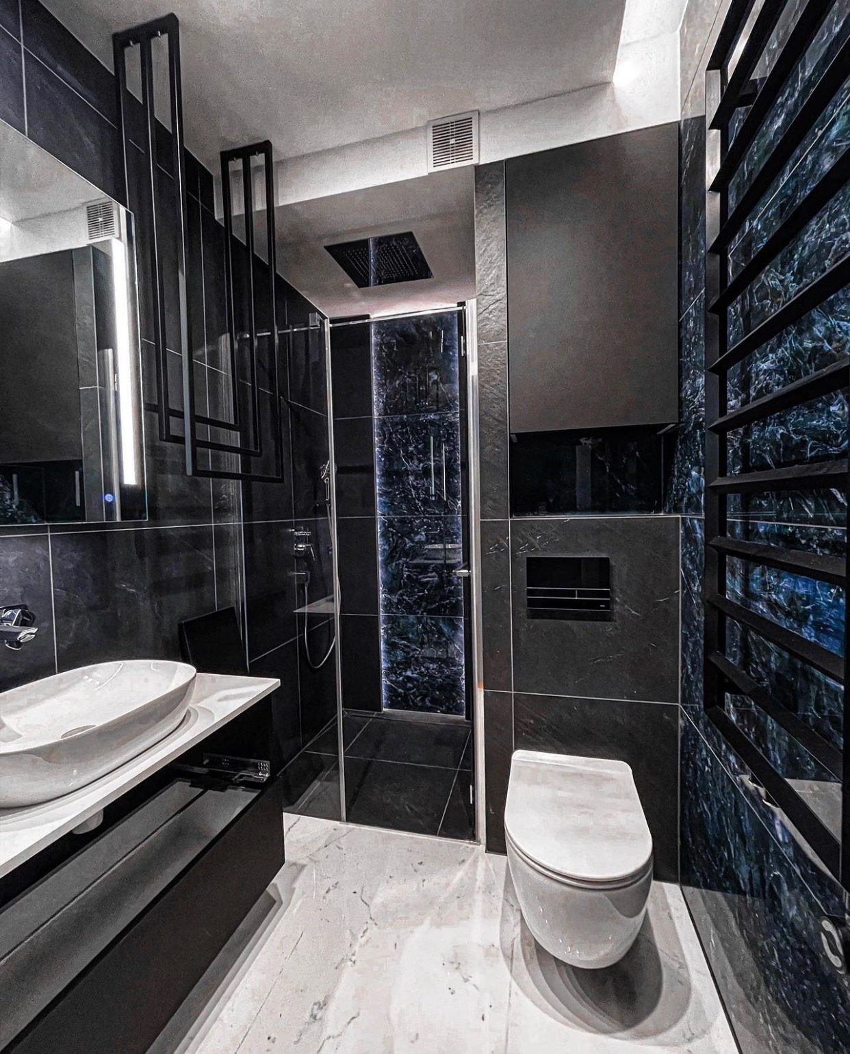 Nowoczesna łazienka z czarnymi płytkami imitującymi marmur, białą umywalką nablatową i kabiną prysznicową z podświetlanym, marmurkowym wzorem na ścianach, oraz dekoracyjnymi, metalowymi elementami...