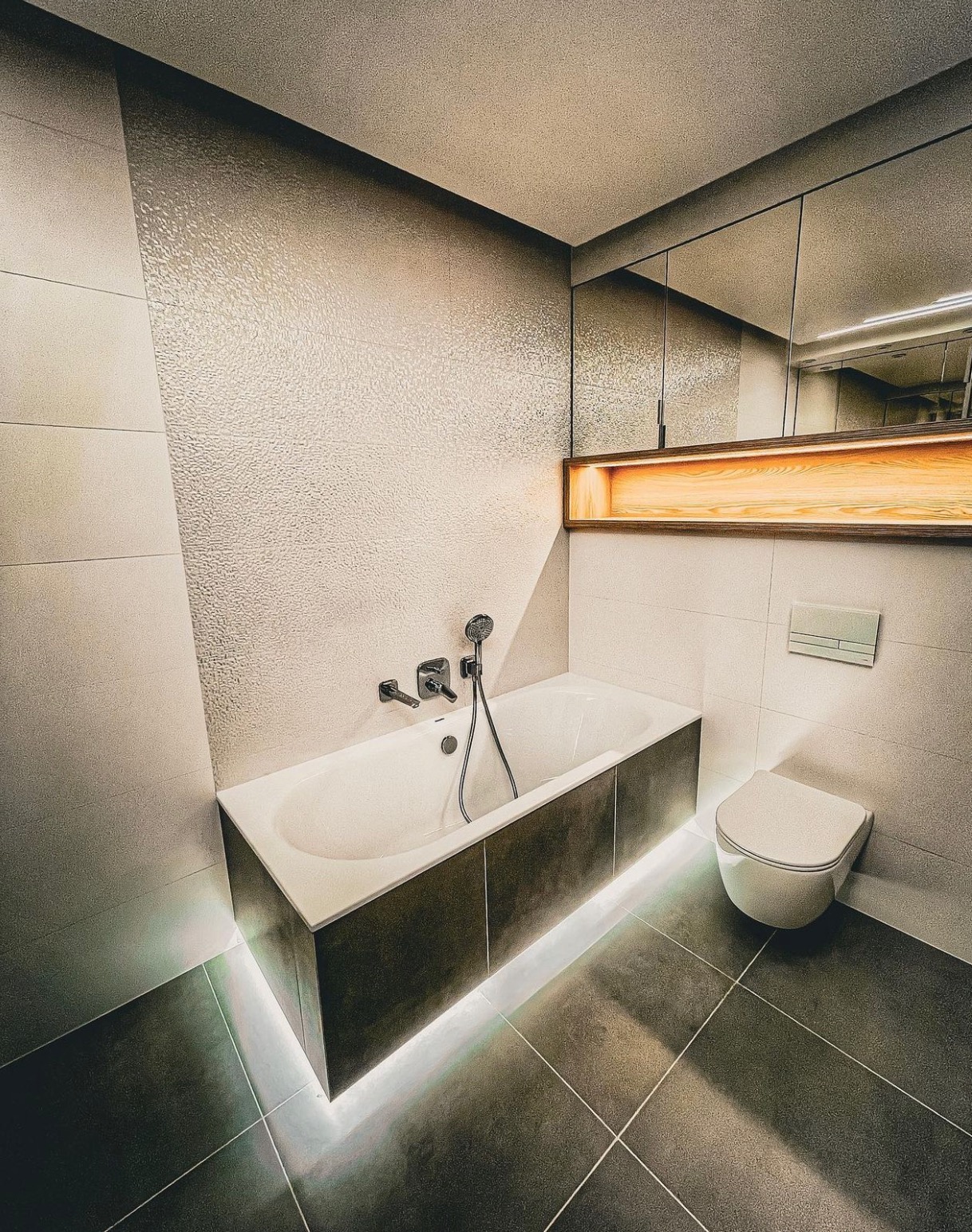 Nowoczesna łazienka z podświetlaną wanną, szarą glazurą i minimalistyczną toaletą.