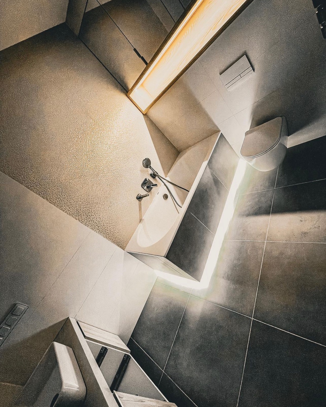 Nowoczesna łazienka z wanną, toaletą i oświetleniem LED, widok z góry pod kątem, ciemne płytki podłogowe i jasna strukturalna ściana.