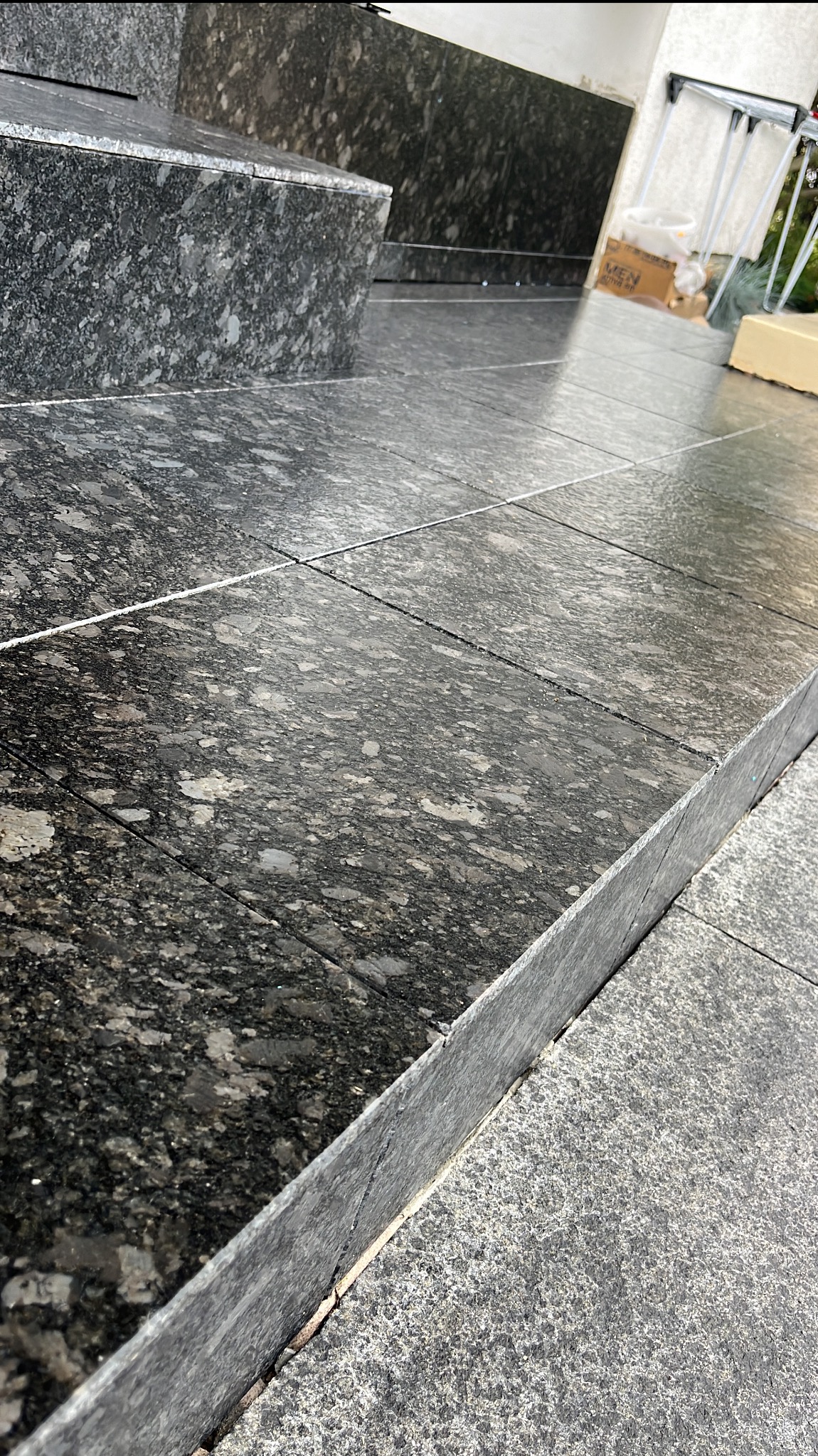 Granitowe płytki podłogowe ułożone na schodach, z widoczną fakturą kamienia i fugami. Fragment schodów granitowych w zbliżeniu, z elementami otoczenia w tle.